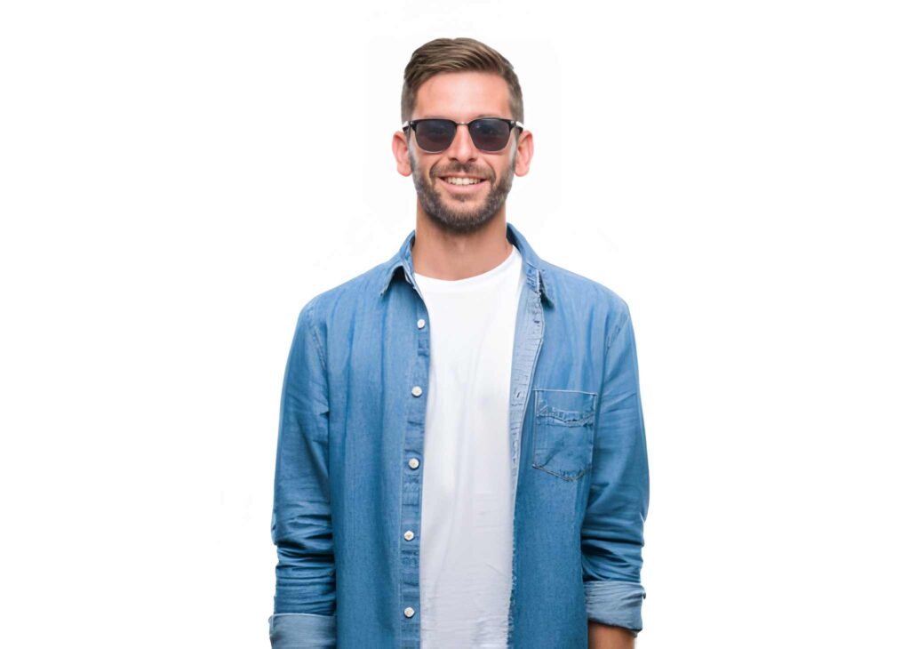 A person stands in front of a white background, wearing a blue denim shirt over a white t-shirt, with arms relaxed at their sides.