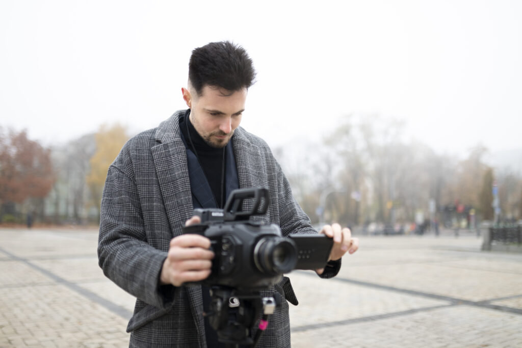 Dolly shot photography angle showcasing a professional videographer adjusting a camera on a tripod in an outdoor setting.