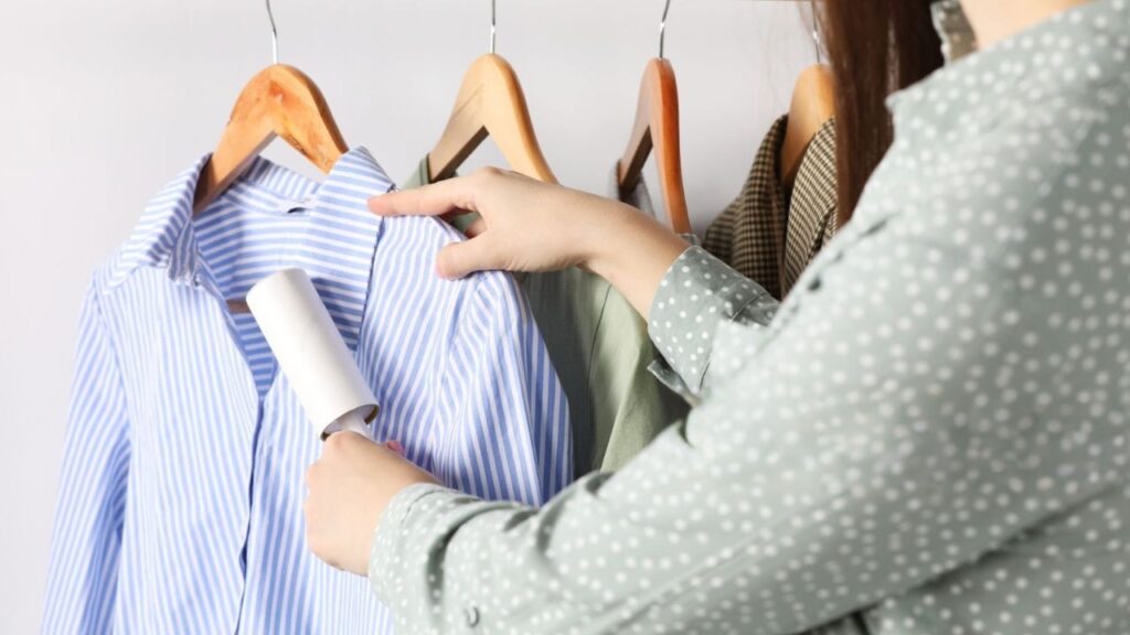 Person using a lint roller on a blue and white striped collared shirt hanging on a wooden hanger.
