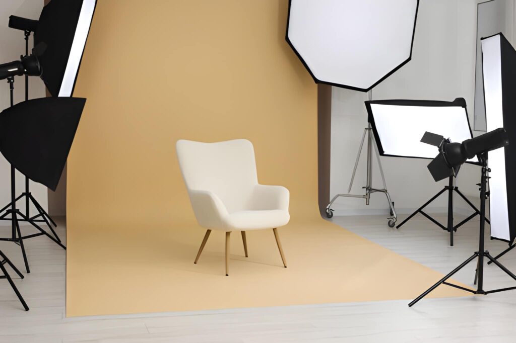 A modern white chair sits on a pale yellow backdrop, framed by various studio lighting equipment.