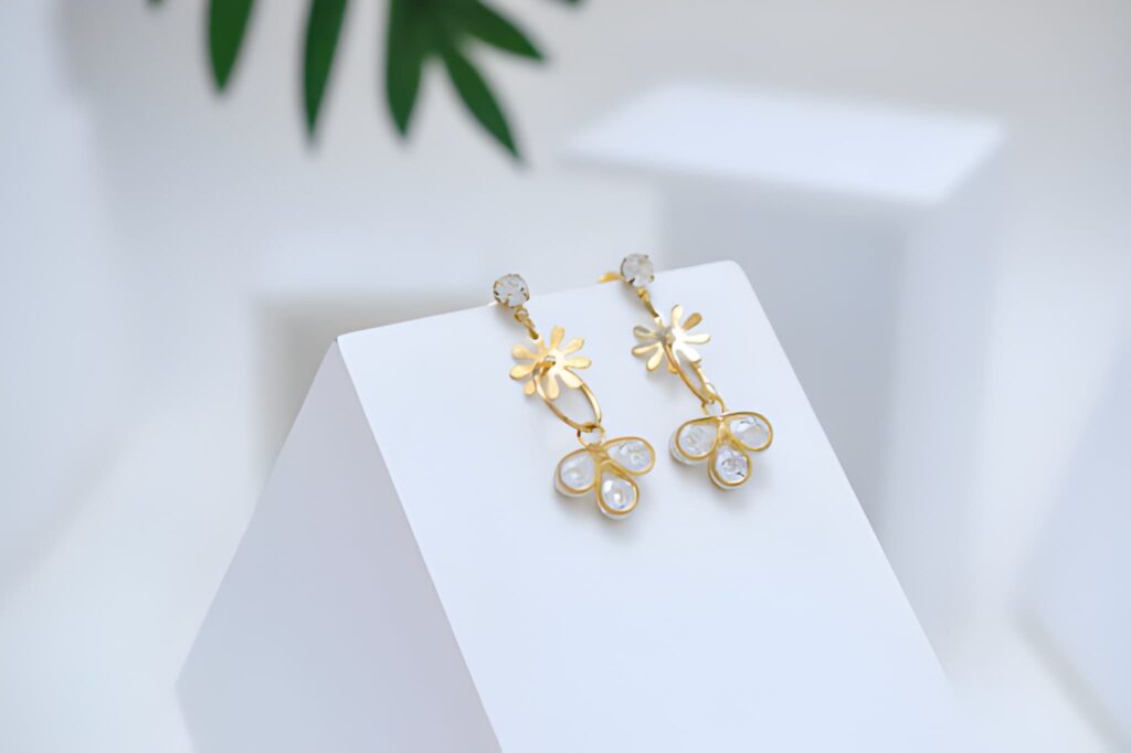 Product shot of gold floral earrings arranged on geometric props, highlighting their sparkle against a clean backdrop.