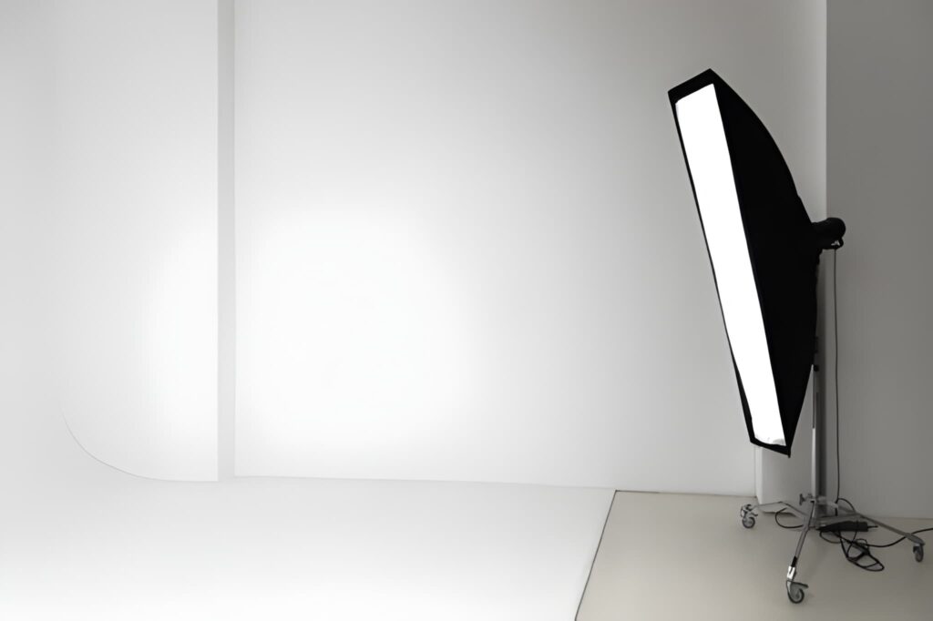 A photography studio setup featuring a large softbox light on a stand in front of a white backdrop and floor.