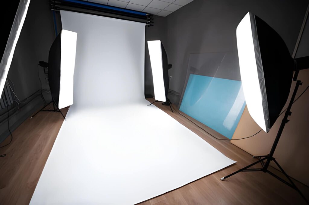 A photography studio featuring a seamless white backdrop, two large softbox lights, and a blue reflector in the background.