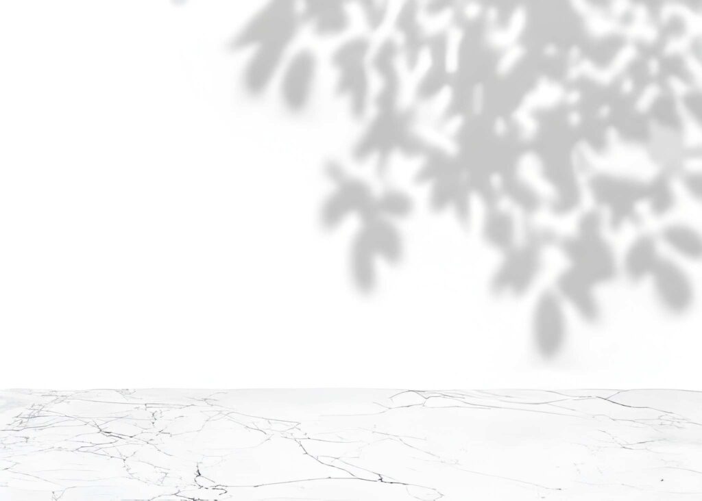 A light, airy scene featuring a marble surface with subtle shadows of leaves cast against a white background.