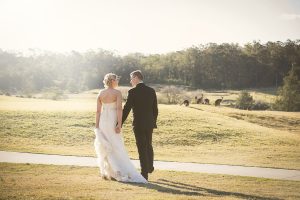 Outdoor wedding photography featuring a bride and groom walking hand in hand along a scenic path with kangaroos in the background.