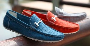 Three blue, red, and grey crocodile pattern loafers are displayed on a wooden rail for shoe photography ideas.