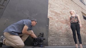 A man taking a picture of a woman in the street with a camera focusing on photography angles.