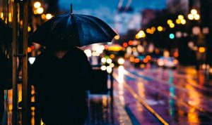 Night photography ideas: a person standing with an umbrella on a road at night.