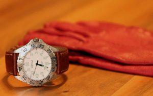 A packshot photograph: mage of orange color gloves and a watch with a brown color leather belt on a table.
