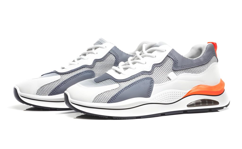 White and gray athletic shoes with mesh panels and a colorful orange heel, designed for comfort and style.