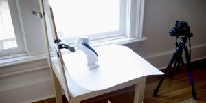 For the jewelry product photography session, there is a camera setup with a tripod and photography props on the table by the window.