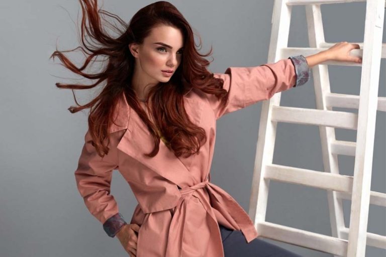Woman in pink trench coat leaning against ladder and the image is before fashion & beauty retouching