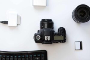 This picture is presenting a camera setup in a flat lay style, which includes a camera, a lens, a memory card, an adopter, and a computer keyboard.