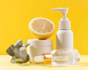 Three organic beauty products are grounded on a light-yellow surface, a piece if lemon is on one bottle and few leaves are beside it, the background is yellow and it showcasing the ingredients as features. 