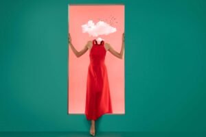 This image is showing a Model, she is wearing red dress, entering into a room through door, one leg is inside the green color room, two hands are on the door, head is full of cloud, the background is pink and it is a photo manipulation. 