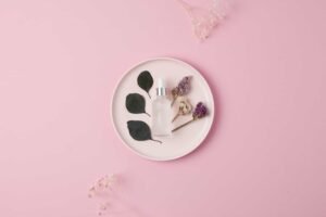 A plate is showing a organic product bottle, it contains leaves, flowers, the background is pink and it is flat lay product photography. 