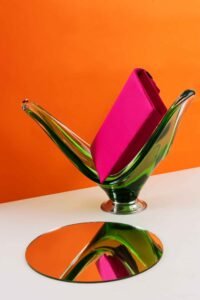 A pink bag is showing on a glass stand, background is orange, a mirror is near the stand and reflection of the bag is shown on the mirror and it is adding personality.