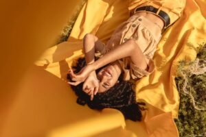 A model is lying on a surface, she is wearing a yellow dress, background is yellow and the shot is taken in a strange way. 