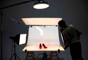 a person standing in front of a 3-light setup with a pair of red shoes on a white surface