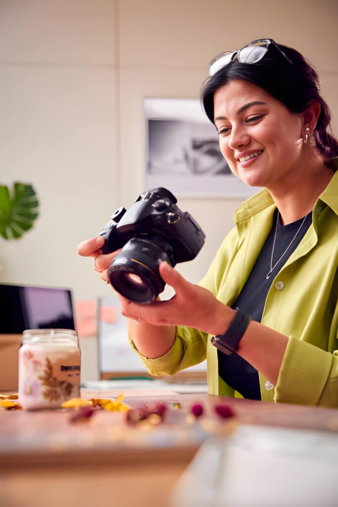 A photographer adjusting camera settings while wearing a green shirt, surrounded by photography gear on a table.
