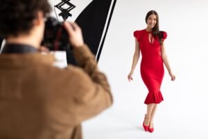 A photographer captures a moment of a woman in a flowing red dress, showcasing her elegance and style in a white background.