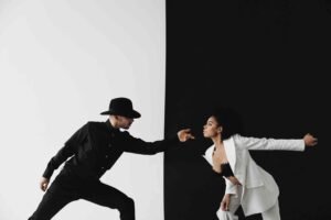 A couple of people that are standing up, where the girl wearing white on a black background and the boy is wearing black on the white background.