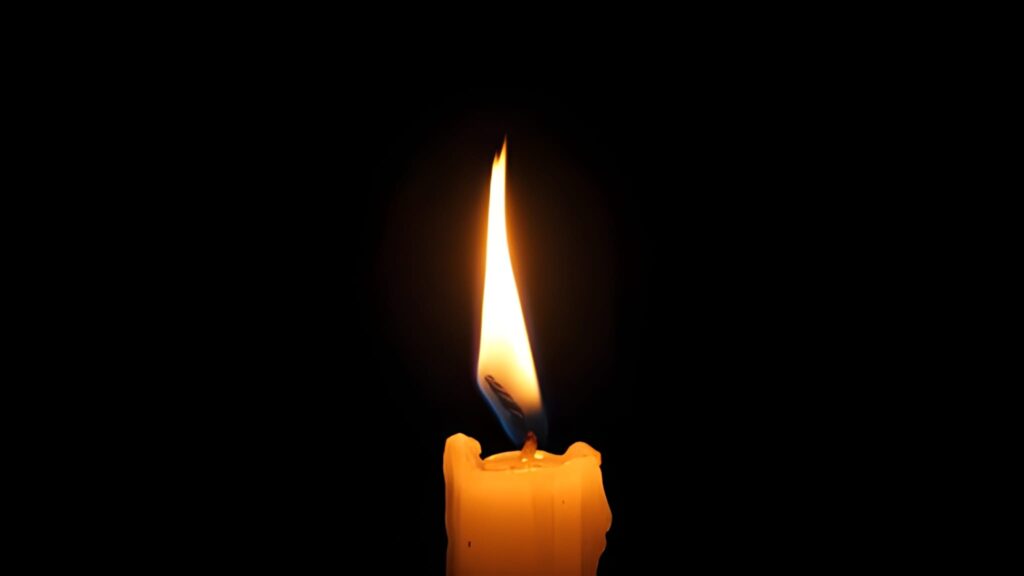 A solitary candle burns brightly against a dark background, its warm flame flickering gently. The scene conveys a sense of calm, warmth, and solitude.