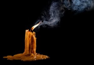 A melting candle with a tall flame and wavy smoke on a black background.