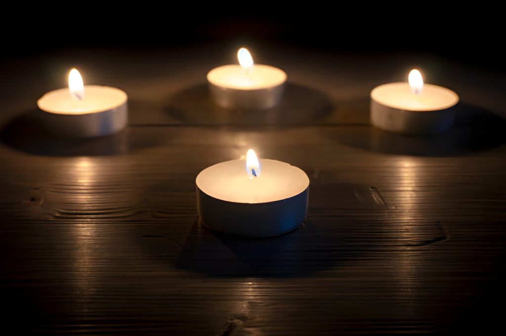 Different angle shooting of four lit tea candles arranged on a dark wooden surface with a calm, cozy mood.