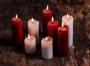 Eight lit candles, four red and four white, arranged on a rough wooden surface.