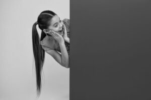 A woman with long hair leans against a wall, exuding a sense of calm and contemplation in her posture. 