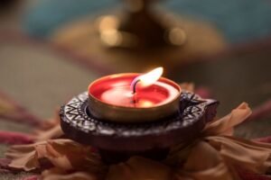 A lit red tealight candle on a carved holder surrounded by flower petals.