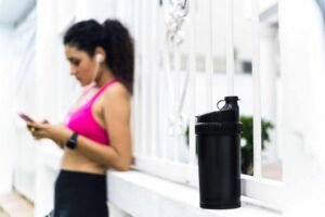 Woman in sportswear using smartphone next to a black water bottle.