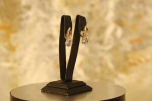 Pair of diamond earrings on a black stand with a golden, blurry background.