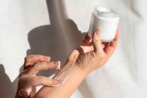 Person applying cream from a jar to forearm, creating a smooth texture on the skin.