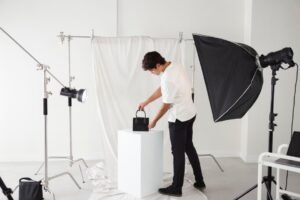 A man with a hand bag poses against a simple white backdrop, prepared for a photography session with best lighting setup.