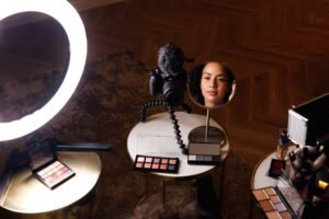 A woman in front of a mirror, smiling and showcasing her makup product with a red background, a camera shows makeup photography.