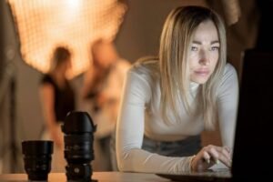 Person working on laptop with camera lenses on table, doing ecommerce photo retouching.