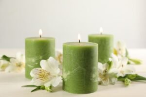 Three lit green candles with white flowers on a wooden surface.