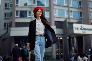 A woman in jeans and a vibrant red beret walks along the street, exuding a sense of casual elegance and confidence.