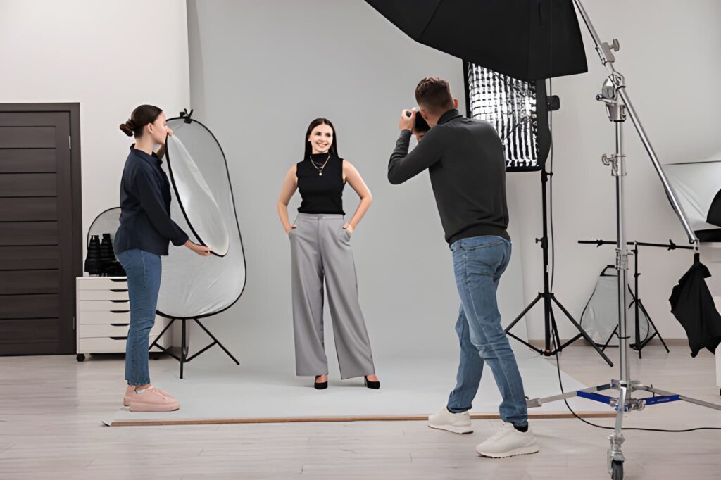 A fashion photoshoot in a studio, featuring a model in stylish attire being photographed, with a stylist adjusting her look for fashion photography.