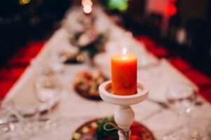 Lit red candle on a white stand at a festive table setting with a blurry background.