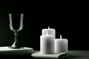 A silver wine glass with three lit white candles on a dark background.