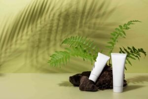 Cosmetic tubes with fern leaves and shadow on a beige background.