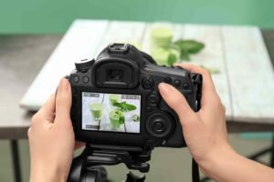 Hands holding a DSLR camera focused on a screen displaying a photo of a drink setup.