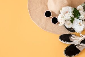 Flat lay product photography display featuring a hat, sunglasses, shoes, and flowers against a vibrant yellow background.