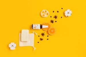 A vibrant yellow background featuring cosmetic products with orange slices, soft cotton, and aromatic spices, creating a warm and inviting scene.