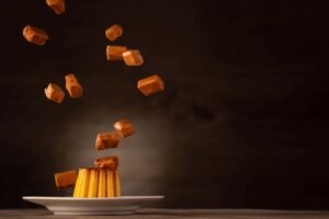 Caramel candies floating above a flan dessert on a white plate with a dark background and warmer lights.