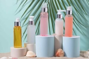 Assorted skincare bottles on pedestals with shells and palm leaves on a teal background.