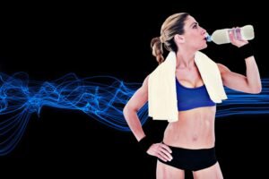 Athletic woman with towel over shoulders drinking water against a black background with blue light streaks.